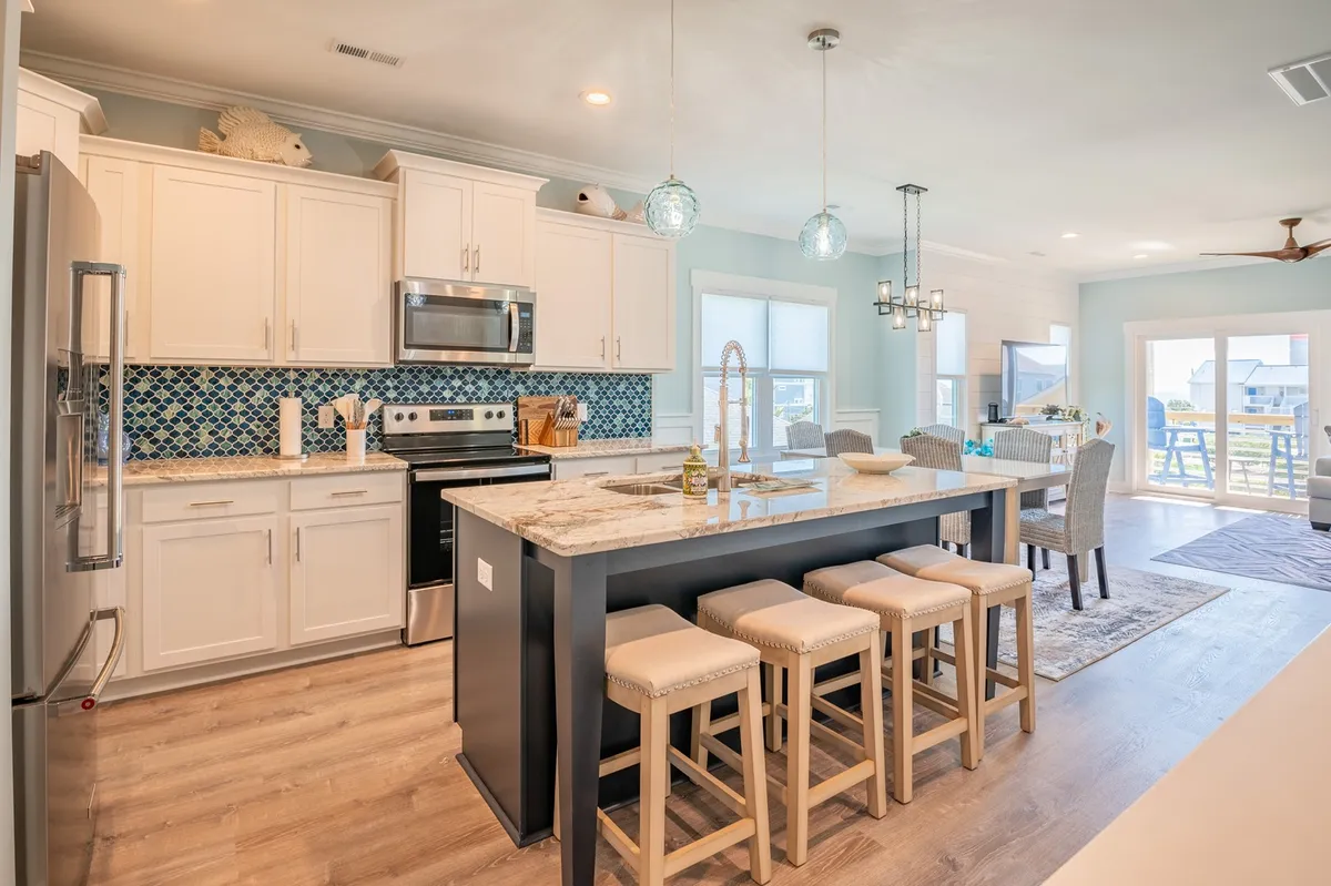 A bright, open kitchen with a central island, blue tile backsplash, modern stainless steel appliances, and stylish pendant lights. The space encourages cooking together, entertaining, and casual family meals, seamlessly blending with the living and dining areas.