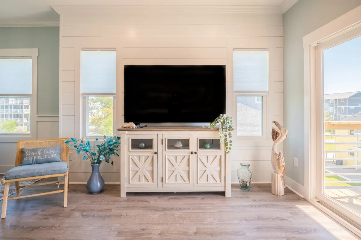 A casual and welcoming entertainment space featuring a television, wooden cabinet, touches of greenery, a sculpture, and a chair. The setup hints at a social atmosphere, ideal for group activities, watching movies, or enjoying downtime between island adventures.