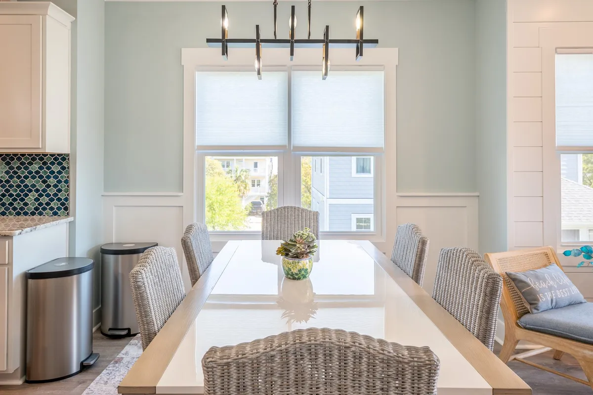 A sunlit dining area with a stylish table, elegant lighting fixture, and a window offering a glimpse of the outdoors. The decorative centerpiece and serene ambiance evoke intimate gatherings and tranquil meals.