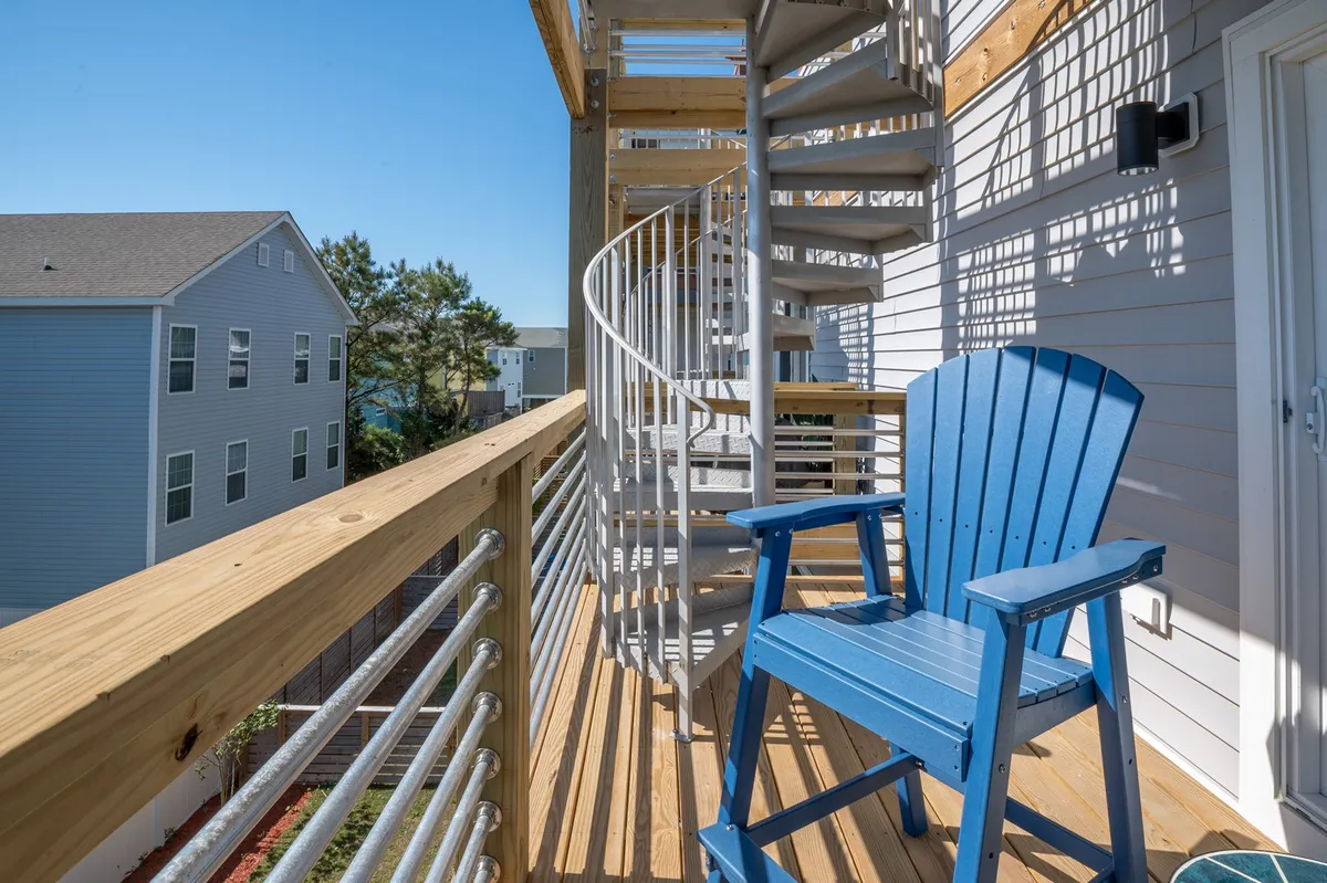 An exterior view highlighting a spiral staircase leading up to a deck furnished with a blue Adirondack chair and wooden railing. The setup encourages relaxation while enjoying panoramic views, with a casual, laid-back vibe ideal for group chats or unwinding with a drink.