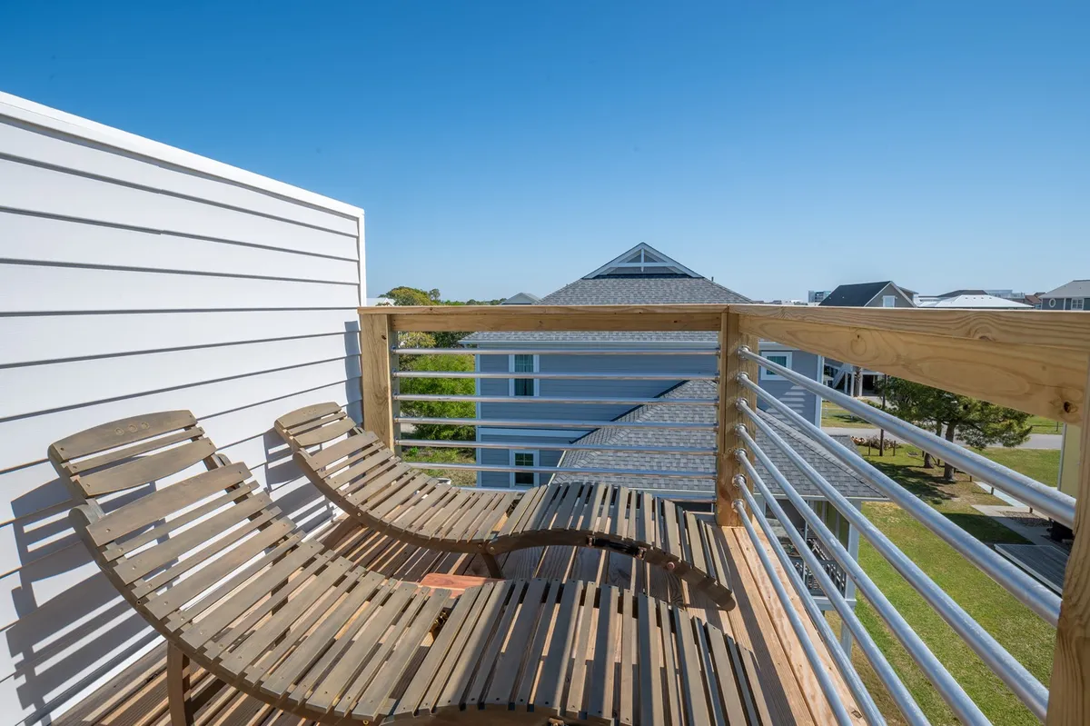 A serene sky deck featuring wooden lounge chairs, a sturdy railing, and sweeping views over the neighboring rooftops and out to the horizon. The setting invites sunbathing, stargazing, or simply taking in panoramic ocean vistas from a private perch.