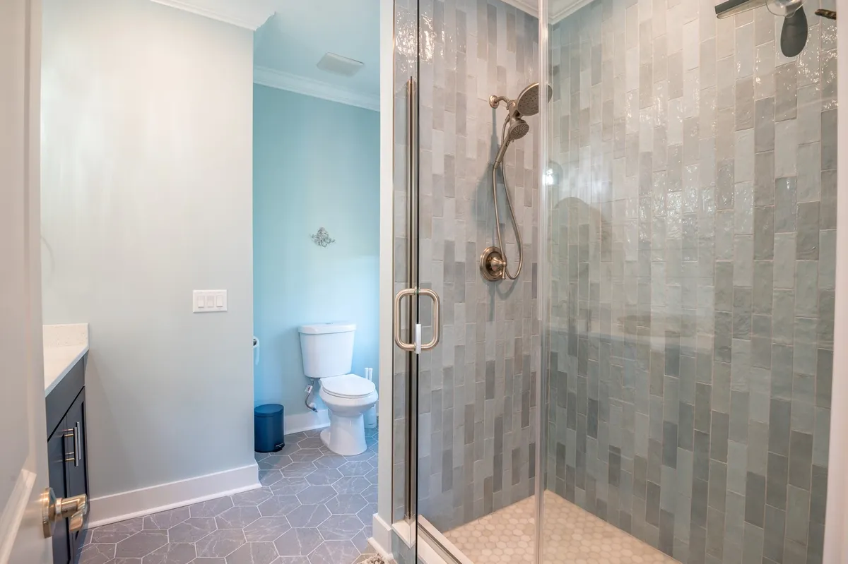 A modern ensuite bathroom with a glass shower enclosure, textured tile wall, and a stylish vanity with sink. The soft color palette and high-end fixtures create a soothing, spa-inspired atmosphere.
