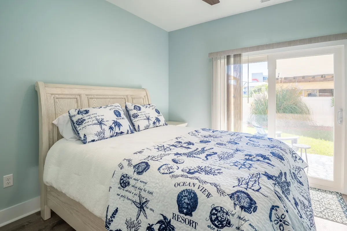 A tranquil bedroom with ocean-themed bedding and a sliding glass door that opens to an outdoor space. The room is bright and inviting, offering a seamless transition between indoor comfort and the fresh air outside.