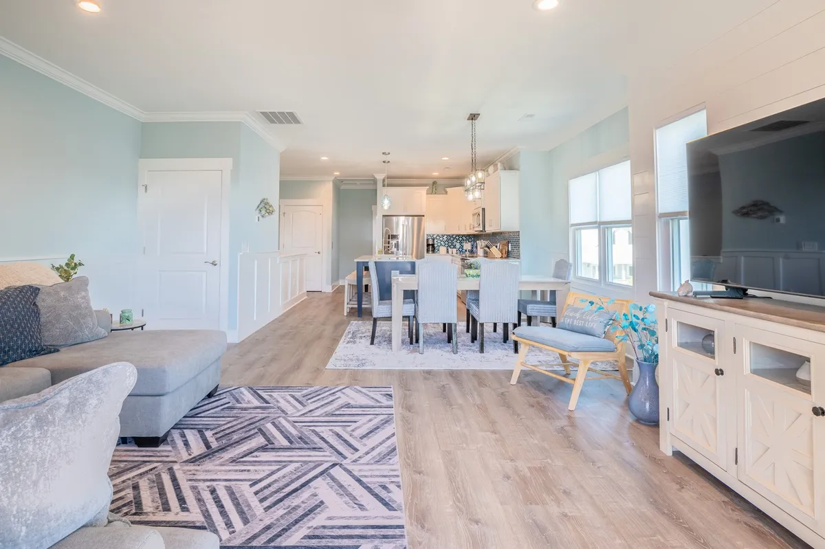 A spacious and inviting great room featuring a comfortable sofa, a dining table set for gatherings, a large television, and a cozy rug that ties the living space together. The room is bathed in natural light, creating a welcoming atmosphere for family and friends to relax, play games, dine, or enjoy movie nights.