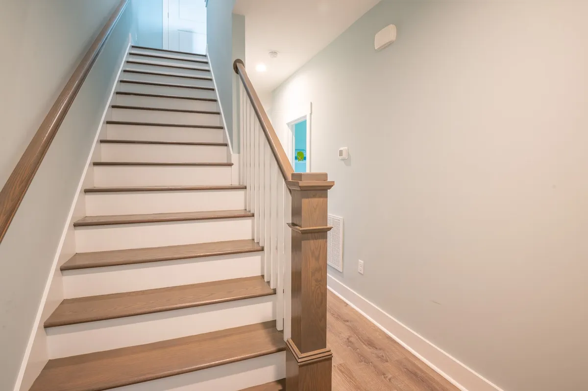 A welcoming staircase with a sleek handrail leads to upper floors, inviting exploration of the home’s various levels. The scene is bathed in soft, natural light, suggesting a journey toward elevated spaces, such as rooftop decks or sky lounges.