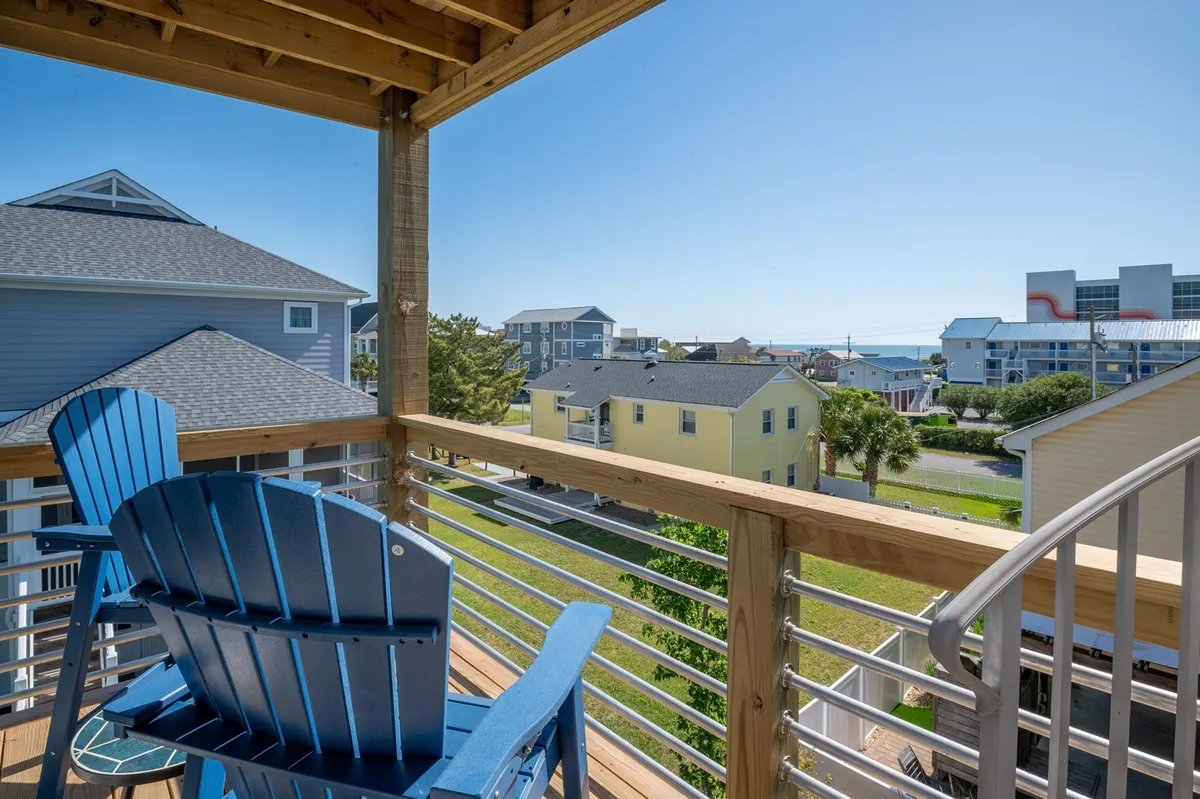 A blue Adirondack chair faces a sweeping ocean view, with nearby homes visible, capturing the tranquil beauty of the coastline and a sense of escape. The setting suggests moments of reflection or socializing after exploring the island's attractions.