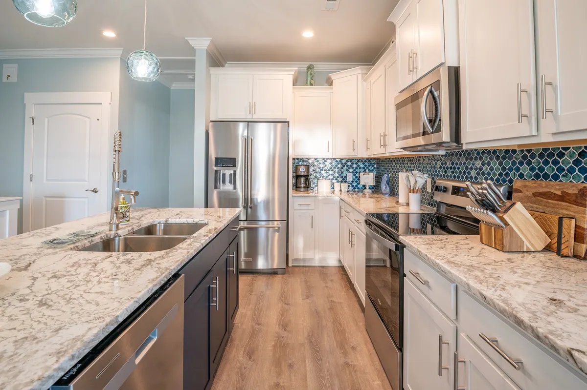 A stylish, modern kitchen featuring granite countertops, stainless steel appliances, and a striking blue tile backsplash. The open layout and ample natural light create an inviting space for culinary experiences and gatherings.