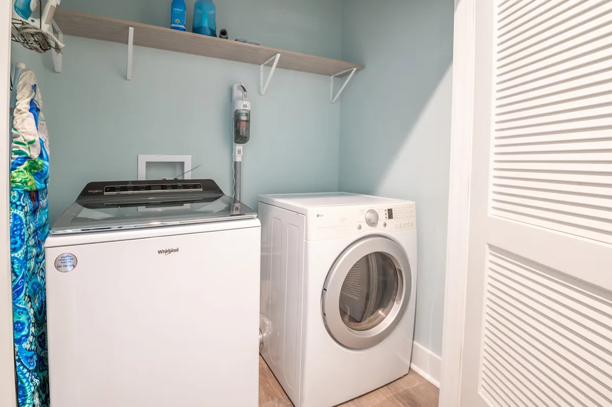 A compact laundry area with a washing machine and dryer, shelves stocked with cleaning supplies, and a tidy, organized setup. The space feels efficient and ready for handling sandy beach towels or family laundry loads.