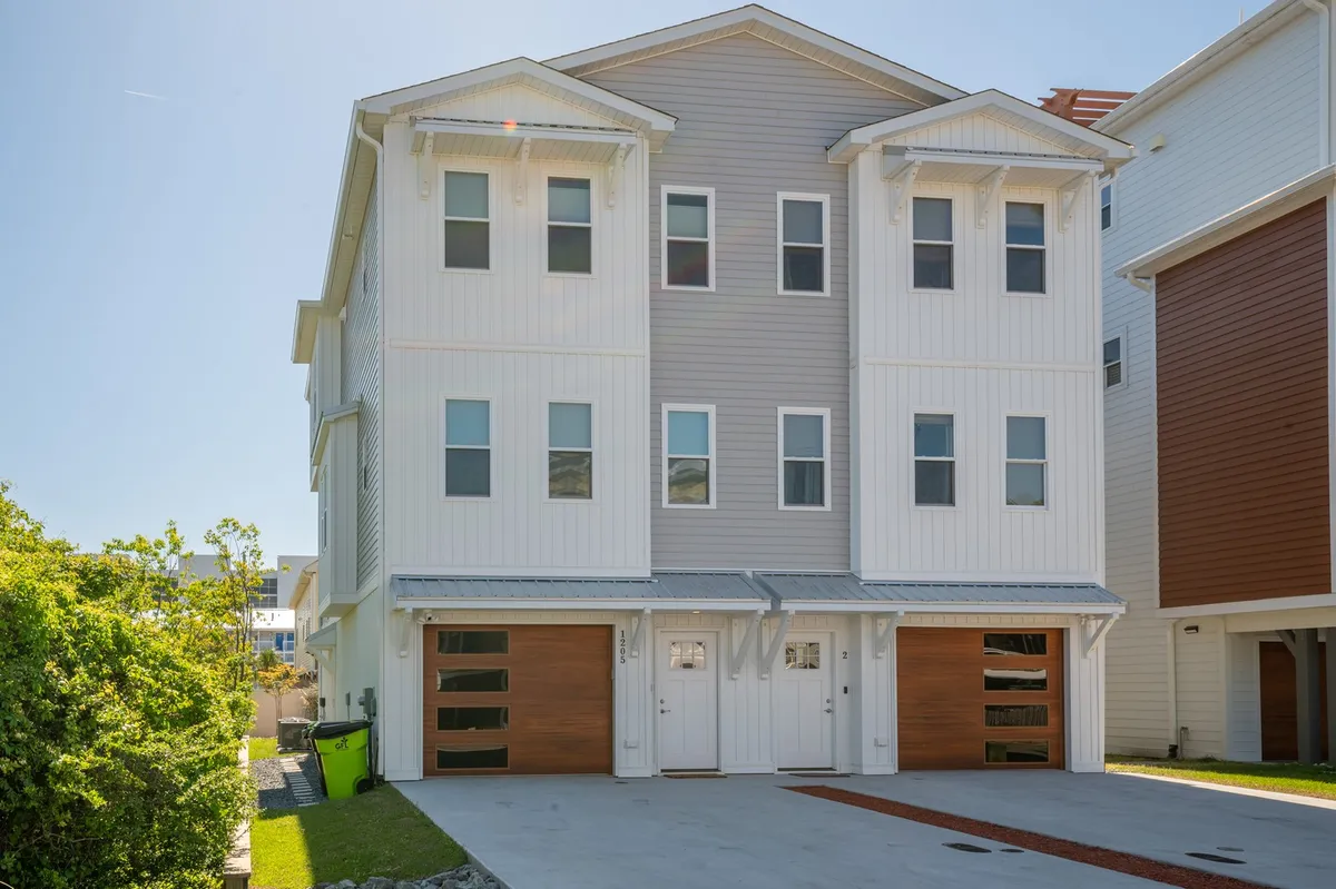 This image showcases the home's modern exterior architecture with inviting wooden garage doors and a clean driveway, set against a welcoming backdrop. The scene hints at parking convenience and the easy transition from the property to outdoor adventures around Pleasure Island.